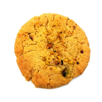 Vue rapprochée d'un cookie Orange Pistachio, parsemé de morceaux de pistache et d'orange confite, offrant une texture granuleuse et croquante.